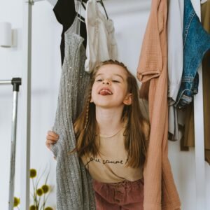 Adorable child playing amidst hanging clothes in closet.